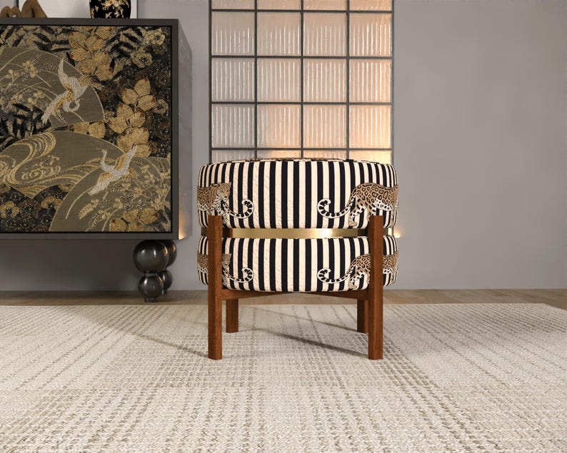 a stylish chair with a black and white striped pattern, placed on a white rug in a room with a large window and a decorative cabinet.