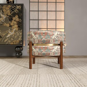 a modern living room with a patterned ottoman, a wooden chair, and a large window with a black and white patterned curtain.
