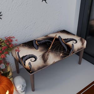 May include: A rectangular bench with a Halloween-themed pattern. The fabric features witch hats, brooms, and spiderwebs in black and gold against a beige background. The bench has four wooden legs.