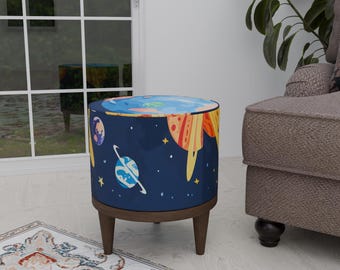 May include: A round, blue and navy blue ottoman with a space-themed design. The ottoman has a wooden base and three legs. The design features planets, stars, and a rocket ship.