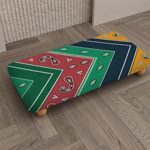 Könnte beinhalten: Ein rechteckiger Hocker mit einem farbenfrohen Paisley-Muster in Rot, Grün, Marineblau und Gelb. Der Hocker hat vier Holzbeine. Das Paisley-Design ist ein klassisches, dekoratives Element.