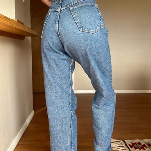 May include: Light blue denim Wrangler jeans. The jeans have a high waist and a straight leg fit. The Wrangler logo is visible on the back waistband. The jeans are worn with a light-colored top.
