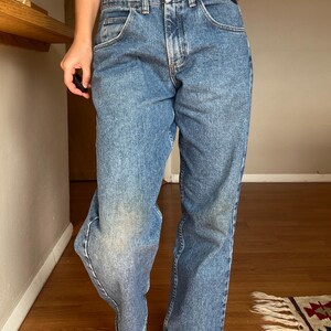 May include: Light blue denim jeans with a classic five-pocket design. The jeans have a straight leg cut and a faded wash, with a button and zipper closure. The jeans are worn and show signs of wear.