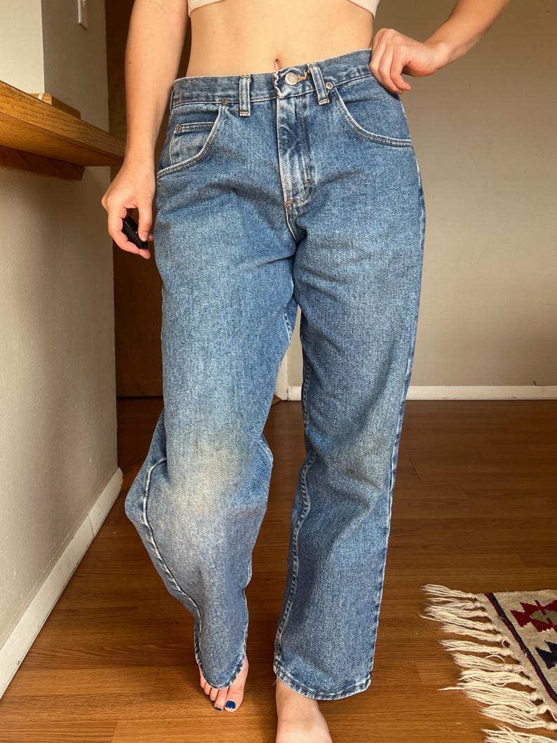 May include: Light blue denim jeans with a classic five-pocket design. The jeans have a straight leg cut and a faded wash, with a button and zipper closure. The jeans are worn and show signs of wear.