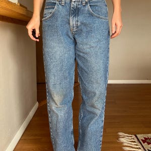 May include: Light blue denim jeans with a classic five-pocket design. The jeans have a button and zipper closure, and a straight leg fit. The denim has a faded wash, giving them a vintage look. The jeans are a casual style.