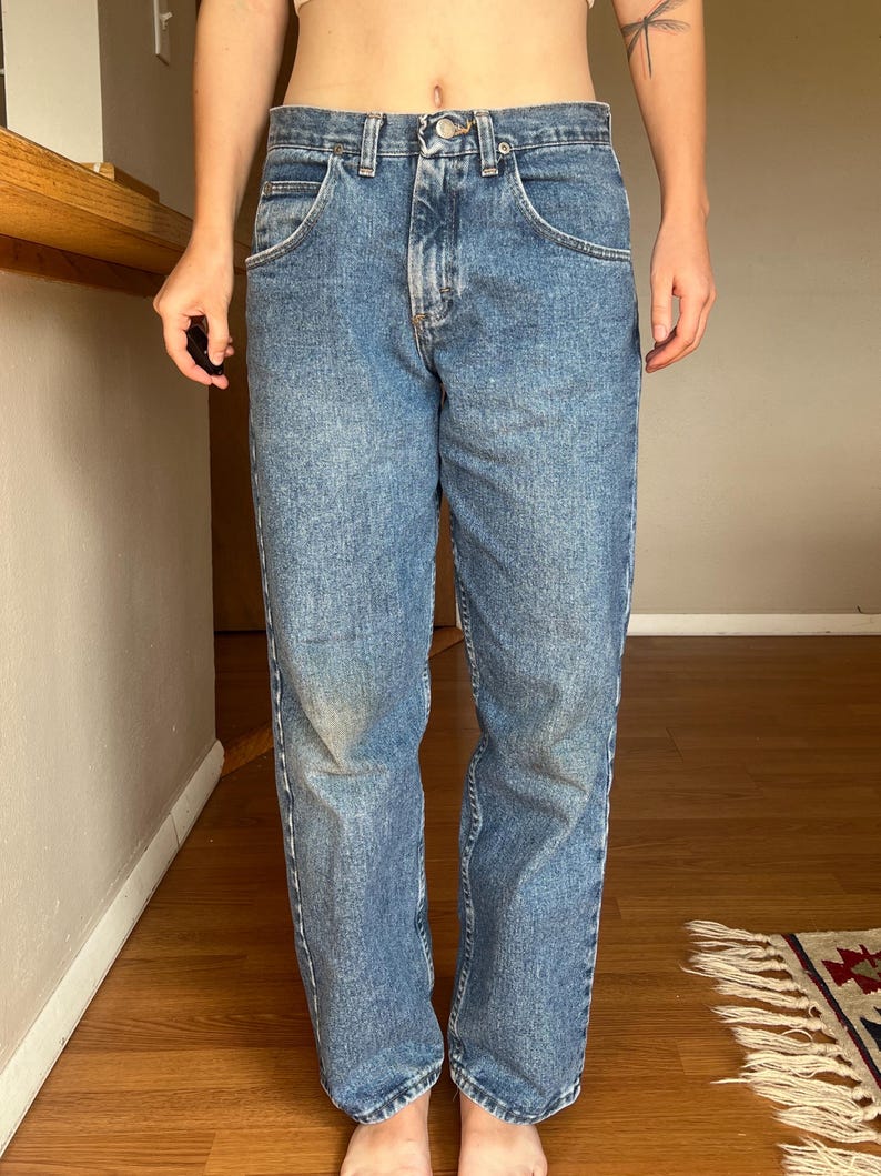 May include: Light blue denim jeans with a classic five-pocket design. The jeans have a button and zipper closure, and a straight leg fit. The denim has a faded wash, giving them a vintage look. The jeans are a casual style.