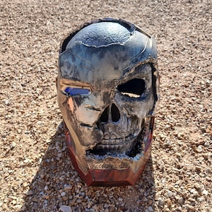 May include: A black, silver and red helmet with a skull design. The helmet is cracked and broken, revealing the skull underneath.