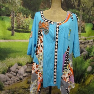 May include: A blue, asymmetrical top with a zipper closure and a patchwork design featuring various colors and patterns, including orange, white, black, and purple. The top has a "LOVE" applique on the front.