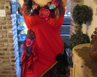 May include: A red dress with black lace and floral embellishments. The dress has a sweetheart neckline and a fitted bodice. The skirt is full and flowing. The dress is on a mannequin and is displayed on a white pedestal.