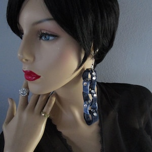 May include: A pair of long, dangling earrings made of denim fabric with silver studs. The earrings are blue and have a chain-like design.