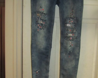 May include: Blue denim jeans with rhinestones and silver embellishments on the legs. The jeans have distressed details and a slim fit.