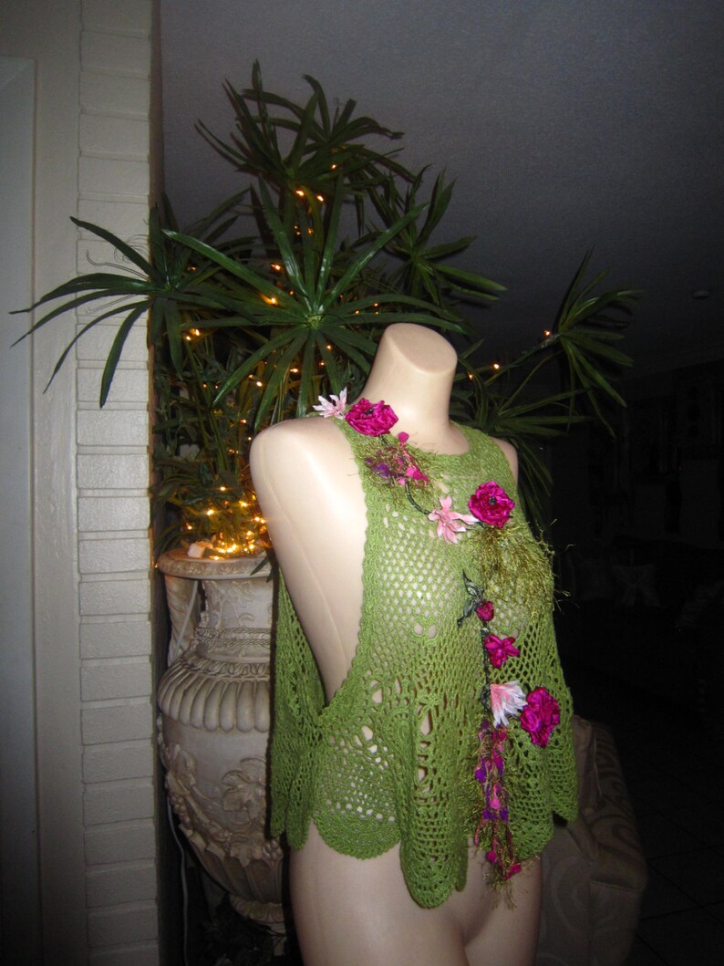 May include: Green crochet top with pink and green floral embellishments. The top is sleeveless and has a loose, flowing fit.
