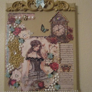 May include: A decorative wall art piece with a vintage aesthetic. It features a framed image of a woman in a black dress, surrounded by flowers, lace, and pearls. A clock with Roman numerals and a butterfly are also included in the design.