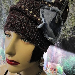 May include: A woman wearing a dark brown knit beanie with a blue denim patch and a silver chain necklace with a flower charm.