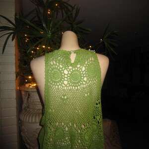 May include: Green crochet top with a delicate pattern. The top is sleeveless and has a round neckline.