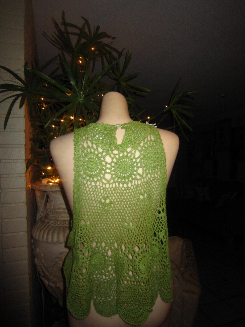 May include: Green crochet top with a delicate pattern. The top is sleeveless and has a round neckline.