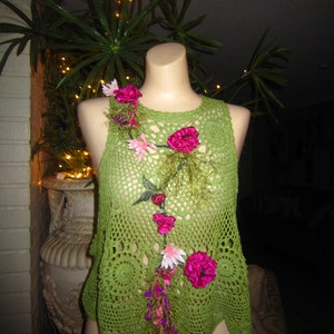 May include: Green crochet top with pink and white flower embellishments. The top has a scalloped hem and a loose fit.