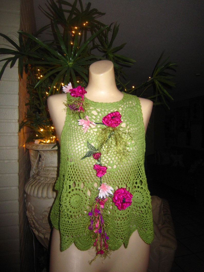 May include: Green crochet top with pink and white flower embellishments. The top has a scalloped hem and a loose fit.
