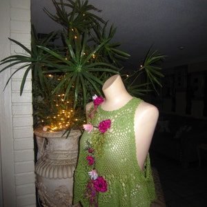 May include: Green crochet top with pink flower embellishments. The top has a loose, flowy fit and a scalloped hem.