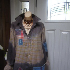 May include: A long-sleeved, plaid shirt with a faded ombre effect. The shirt has been repurposed with patches of different fabrics, including denim and lace. The denim patch on the bottom right pocket has the word "LOVE" embroidered on it.