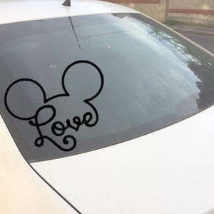Puede incluir: Calcoman&iacute;a de vinilo negro con las orejas de Mickey Mouse y la palabra "Love" en cursiva. La calcoman&iacute;a est&aacute; aplicada en la ventana trasera de un coche blanco. Un dise&ntilde;o popular para accesorios de coche.