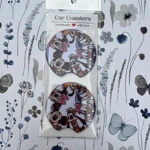May include: Two car coasters featuring Mickey Mouse, Minnie Mouse, Donald Duck, and Goofy. The coasters are white with a colorful cartoon design and are packaged in a clear plastic sleeve. The text "Car Coasters Handmade with love" is printed on the packaging.