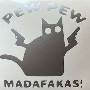 May include: A silver graphic of a cat silhouette holding two guns, with the words "PEW PEW" above and "MADAFAKAS!" below. The design is set against a white background, creating a striking contrast.