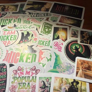 Op de afbeelding: Een verzameling diverse stickers met afbeeldingen en tekst gerelateerd aan de musical Wicked, waaronder karakterillustraties, iconische symbolen zoals heksenhoeden en bezems, en citaten zoals In My Popular Era en Wicked, in diverse vormen.