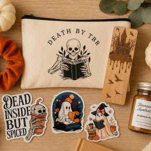 May include: A canvas zipper pouch with a skeleton reading a book and the text DEATH BY TBR, a wooden bookmark with a haunted house, three stickers featuring ghosts and a coffee cup, a rust-colored velvet scrunchie, and a jar of pumpkin roll candle.