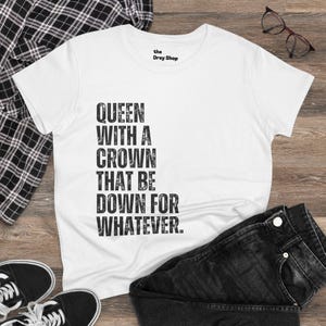 Op de afbeelding: Wit T-shirt met een verweerde zwarte grafische afbeelding met de tekst "Queen with a crown that be down for whatever." Het Dray Shop logo staat bovenaan in het midden van het shirt.