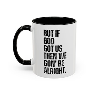 May include: White ceramic coffee mug with a black handle and black rim. The mug has a black inspirational quote that reads "But if God got us then we goin' be alright."