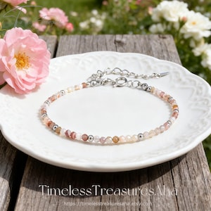 May include: A delicate bracelet featuring small, faceted, multi-colored gemstone beads in shades of pink, peach, and clear, interspersed with tiny silver-toned metal beads. The bracelet includes a silver-toned metal chain extender and a clasp.