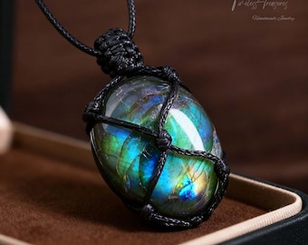 May include: A handcrafted necklace featuring a large, iridescent labradorite gemstone pendant. The stone is encased in a woven black cord, suspended from a matching cord. The gemstone displays a vibrant play of colors, including blues, greens, and yellows.