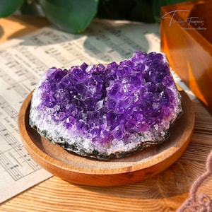 Könnte beinhalten: Ein großer Amethyst-Kristall-Cluster in tiefem Lila. Der Kristall liegt auf einem Holz-Untersetzer.