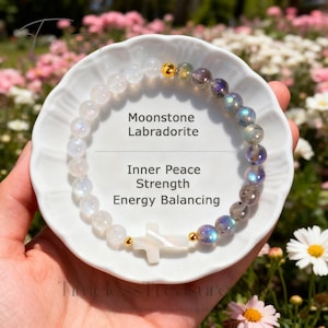 May include: A beaded bracelet featuring moonstone and labradorite gemstones. The bracelet includes a white cross charm and gold-colored accents. Text on the plate reads "Moonstone Labradorite" and "Inner Peace Strength Energy Balancing."