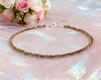 May include: A gold-coloured beaded anklet with a silver clasp, displayed on a pink and white fabric. The anklet features small, faceted beads. A bouquet of pink and white roses is in the background. The text "TimelessTreasuresAha" is at the bottom.