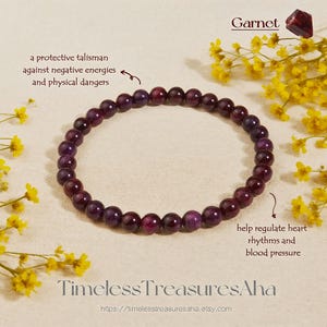 Könnte beinhalten: Ein Armband aus tiefvioletten Granatperlen, das als schützender Talisman beschrieben wird. Das Bild enthält das Wort "Garnet" und den Text "Timeless TreasuresAha". Das Armband besteht aus kleinen, runden Perlen.