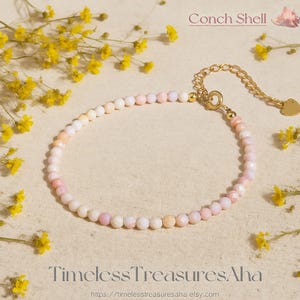 May include: A delicate bracelet featuring small, faceted conch shell beads in shades of pink, peach, and white. The bracelet has a gold-colored chain and clasp, with a small heart-shaped charm. The text "Conch Shell" and "TimelessTreasuresAha" are visible.