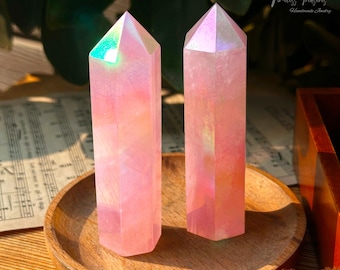 May include: Two iridescent pink crystal points with a rainbow sheen. The points are on a wooden coaster.