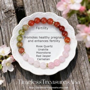 Puede incluir: Una pulsera de cuentas rojas, rosas y verdes, exhibida en un plato blanco. El plato tiene el texto "Fertilidad" y "Promueve un embarazo saludable y mejora la fertilidad". La pulsera está hecha de cuarzo rosa, unakita, piedra lunar, jaspe rojo y cornalina.