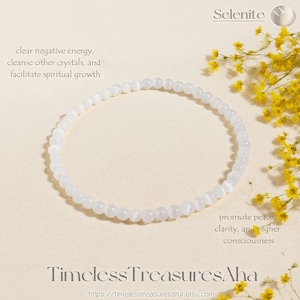 May include: A white beaded bracelet made of Selenite stones. The bracelet is circular and sits on a light beige surface, with text that reads "clear negative energy, cleanse other crystals, and facilitate spiritual growth". The text "Timeless TreasuresAha" is also visible.
