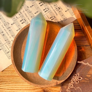 May include: Two iridescent opal crystal points, one light blue and one yellow, are displayed on a wooden bowl. The points are smooth and polished, with a slight shimmer.