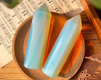May include: Two iridescent opal crystal points, one light blue and one yellow, are displayed on a wooden bowl. The points are smooth and polished, with a slight shimmer.