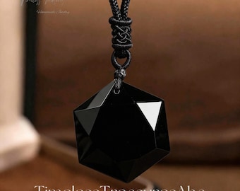 Puede incluir: Colgante de piedra preciosa negra facetada con diseño geométrico, suspendido de un cordón negro. El colgante tiene una superficie pulida y reflectante y un acento triangular blanco. El nombre de la tienda Etsy "Timeless Treasures Aha" se muestra en la parte inferior.