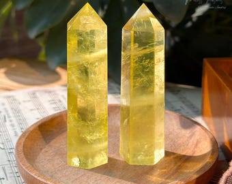 May include: Two yellow citrine crystal points on a wooden plate. The points are about 4 inches tall and have a clear, glassy appearance.