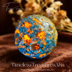 May include: A round, colorful rock with a blue and orange speckled pattern. The rock has a smooth surface and is illuminated with bright orange and yellow hues. The text "Timeless Treasures" is visible in the image.