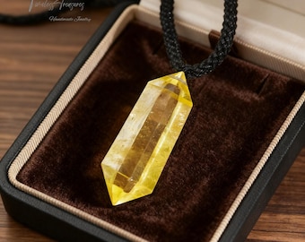 May include: A yellow crystal pendant necklace displayed in a black jewelry box with a brown velvet interior. The necklace has a black cord with gold accents. The box is open, revealing the pendant's shape and color. The text "Timeless Treasures Handmade Jewelry" is visible.