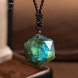 May include: A hexagonal pendant necklace with a labradorite gemstone. The stone displays iridescent blue and green hues. The pendant is suspended from a brown cord. The text "Timeless Treasures Handmade Jewelry" is in the upper left corner.
