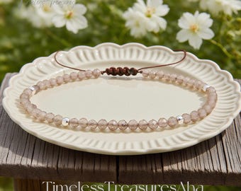 May include: A delicate beaded bracelet with faceted, light-colored beads and silver accents. The bracelet is displayed on a white, scalloped-edge plate, with the text "Timeless Treasures Aha" and a website address visible.