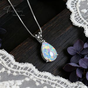 May include: A silver necklace with a pear-shaped opal pendant. The opal displays a vibrant array of colors, including blue, yellow, and pink. The pendant is set in a silver bezel and hangs from a delicate chain. The image includes the text "Timeless Treasures, Handmade Jewelry."